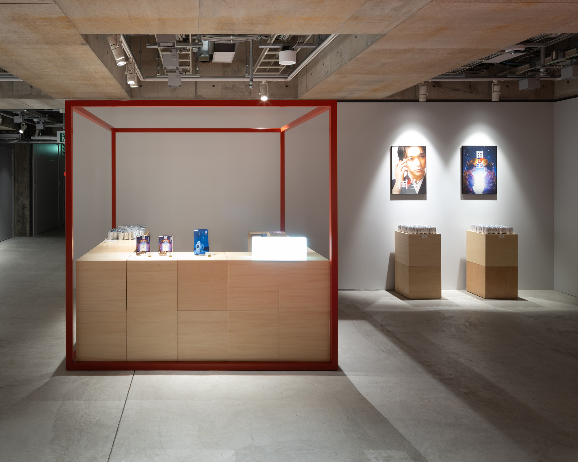 A combined exhibition and shop area with wooden counters displaying merchandise, surrounded by posters installed on the gallery walls.